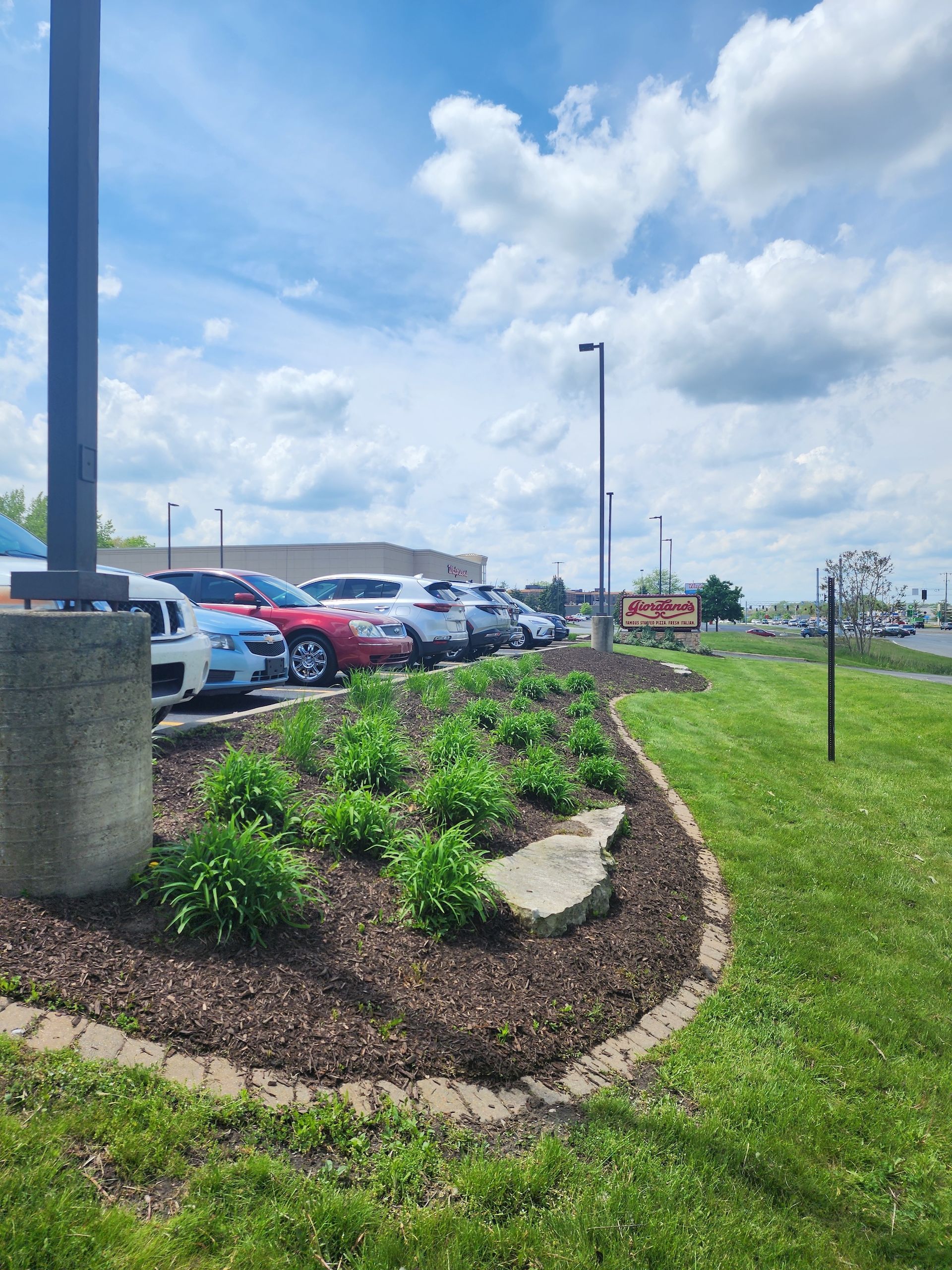 Landscaped flower bed with rocks beside a parking lot under a cloudy sky