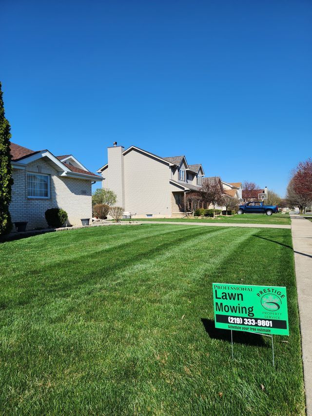 Suburban lawn with rows of houses under a blue sky and a green lawn mowing sign in the foreground