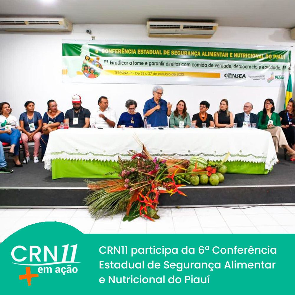 Mesa de conferência com várias pessoas sentadas e banner sobre segurança alimentar em auditório.
