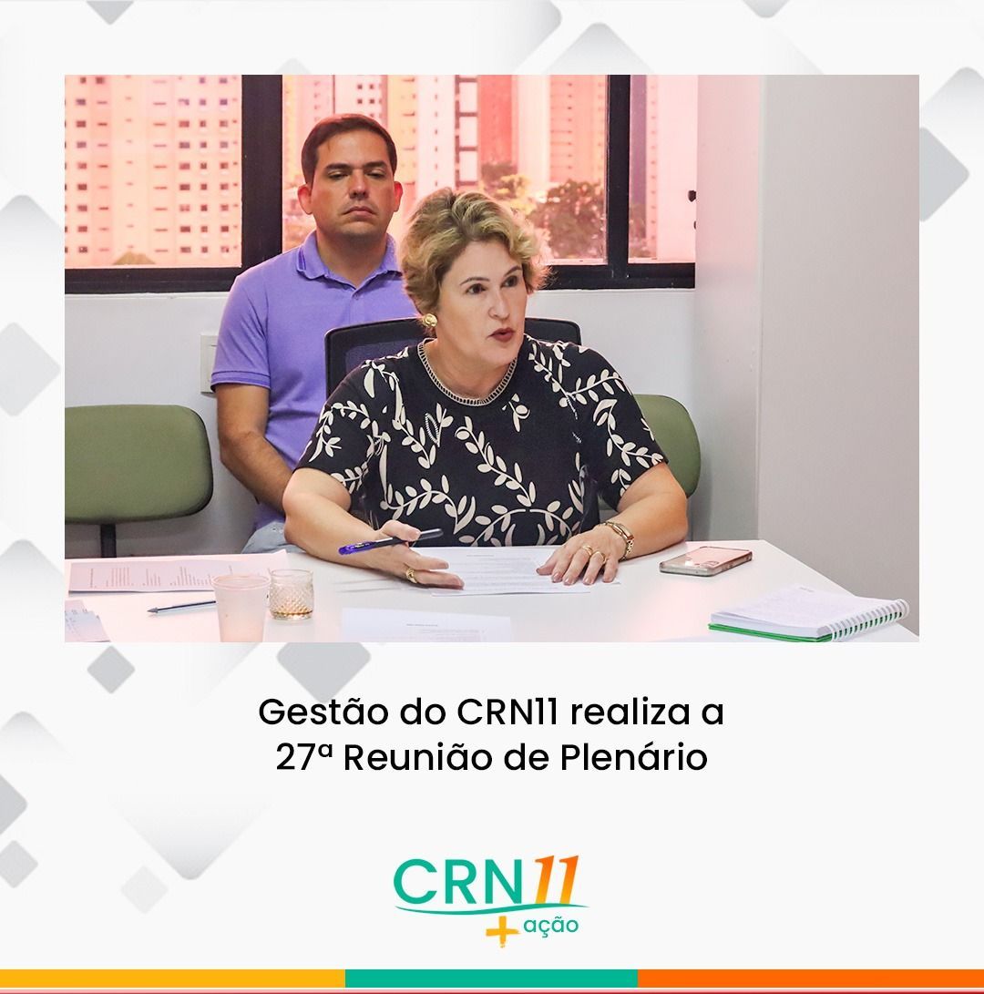 Reunião do CRN11: mulher fala à mesa, com homem sentado ao fundo em sala de plenário.
