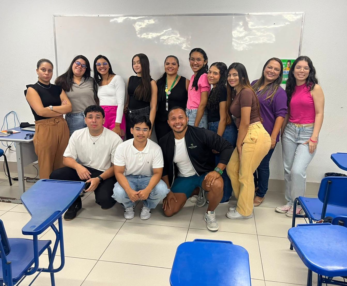 Grupo de pessoas posando em uma sala de aula, com carteiras e cadeiras em primeiro plano.