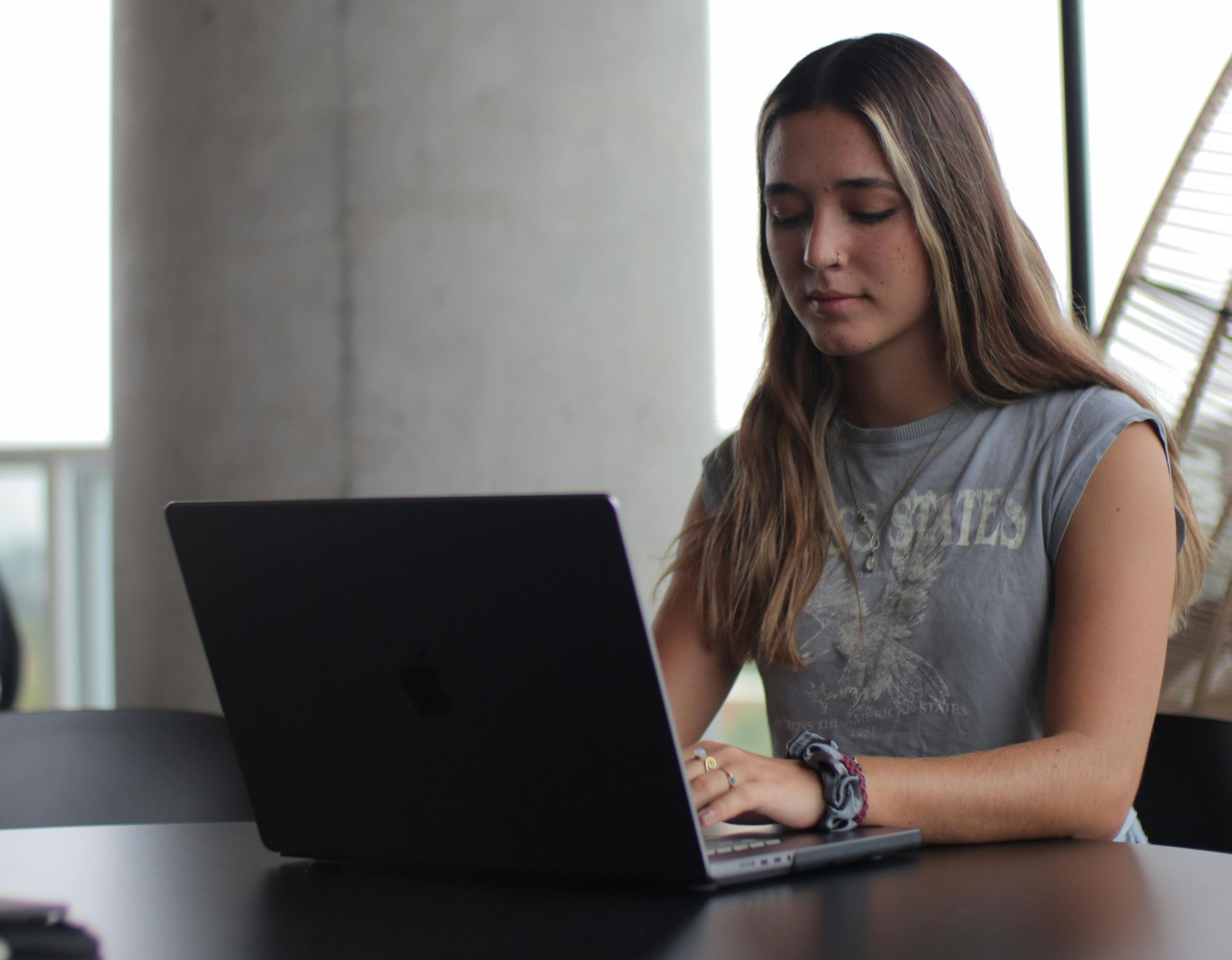 Mulher trabalhando em um laptop em uma mesa em um espaço interno bem iluminado.