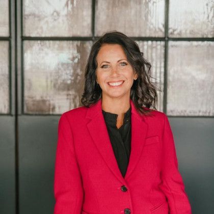 Woman in red blazer smiles in front of glass window.