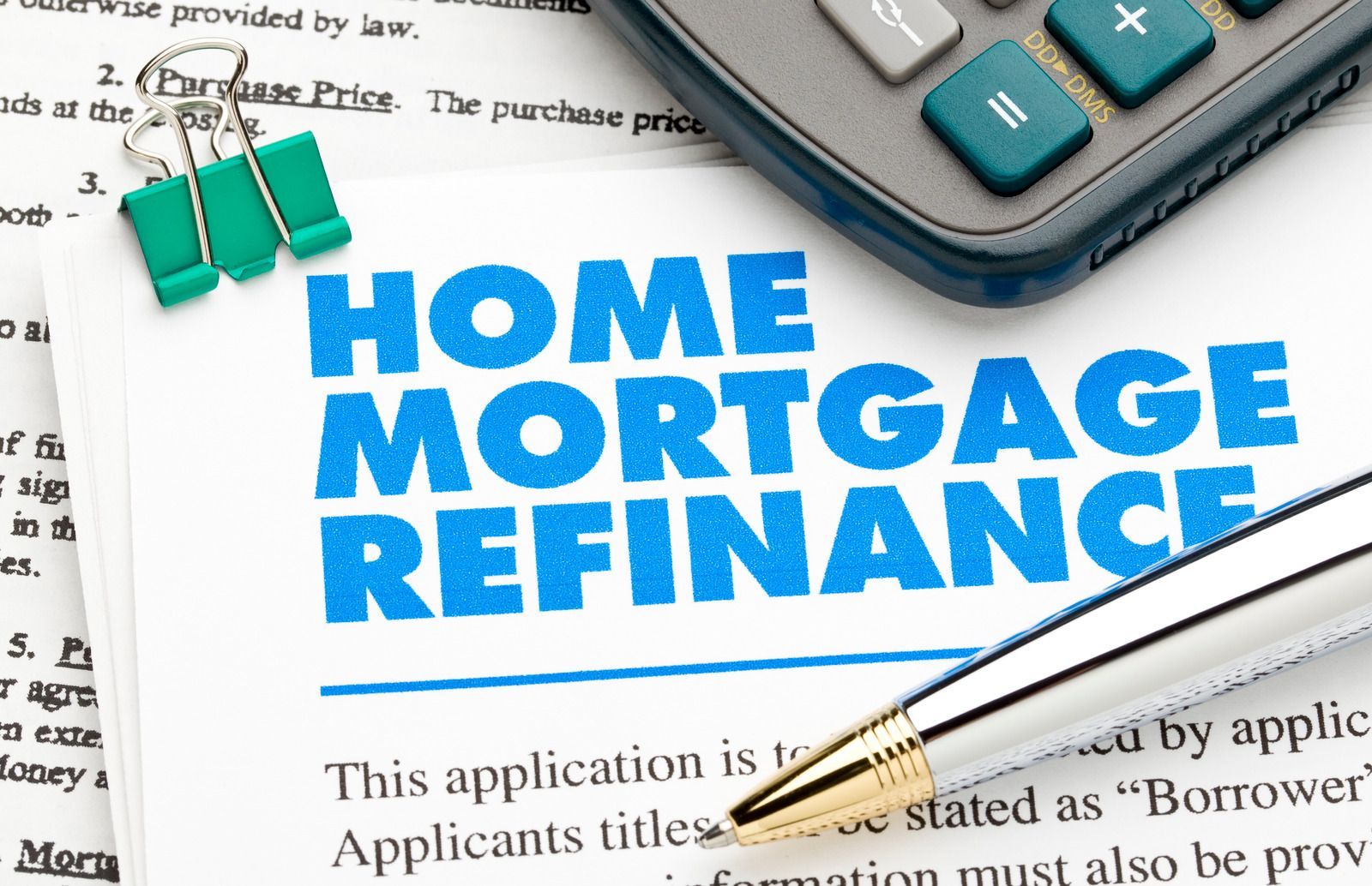 Home mortgage refinance application with calculator, pen, and binder clips.