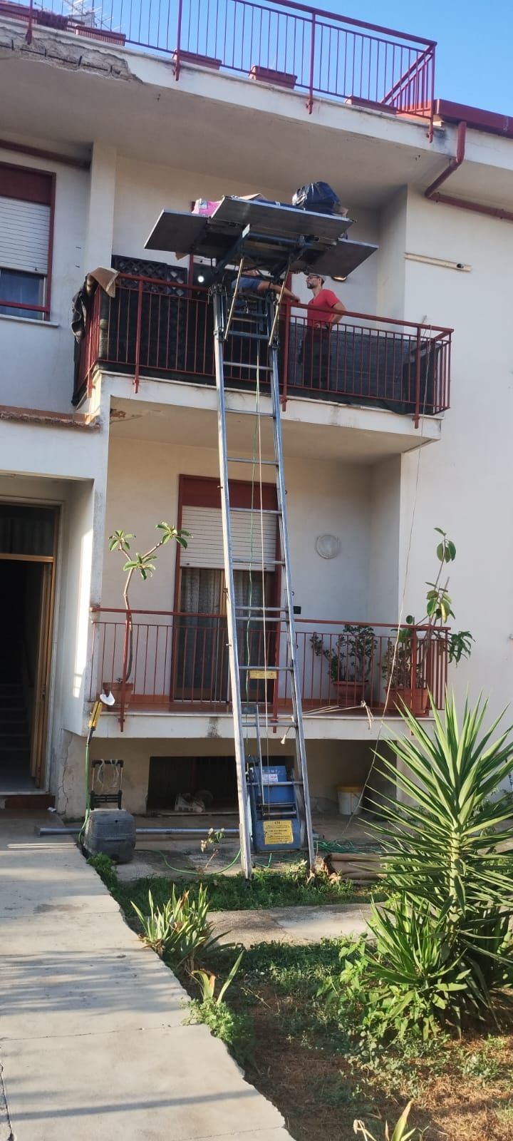 Una piattaforma elevatrice è installata vicino a un edificio con balconi. Una persona è in piedi sulla piattaforma.