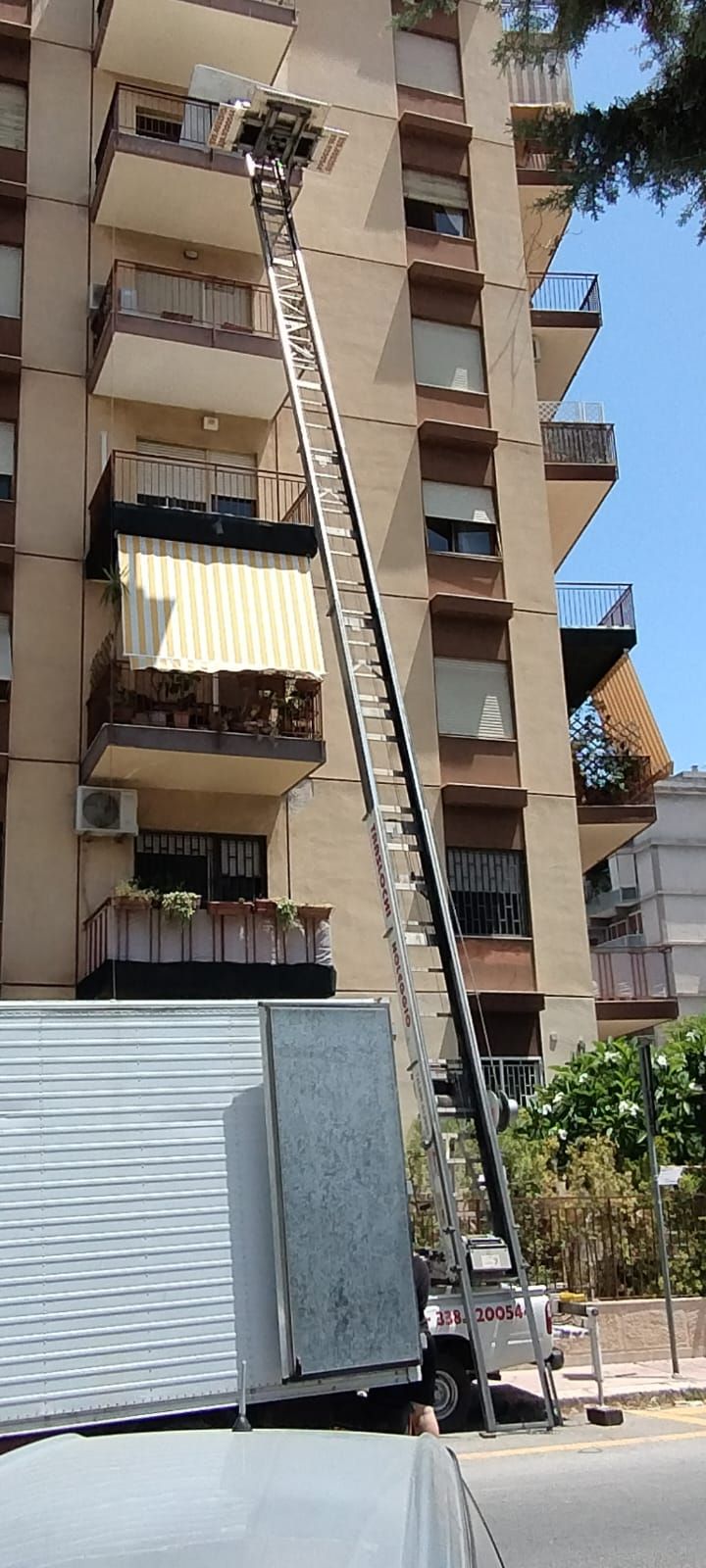 Un edificio alto con un camion per traslochi che solleva i mobili a un piano superiore tramite un ascensore meccanico.