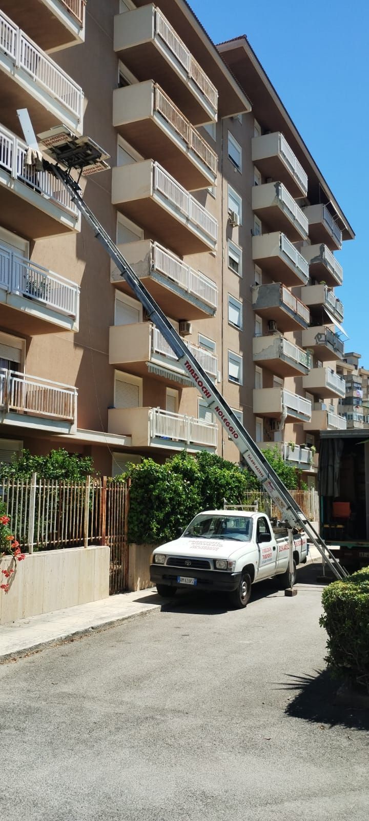 Camion per traslochi che scarica mobili da un edificio con montacarichi. Camion bianco e montacarichi contro un edificio a più piani.