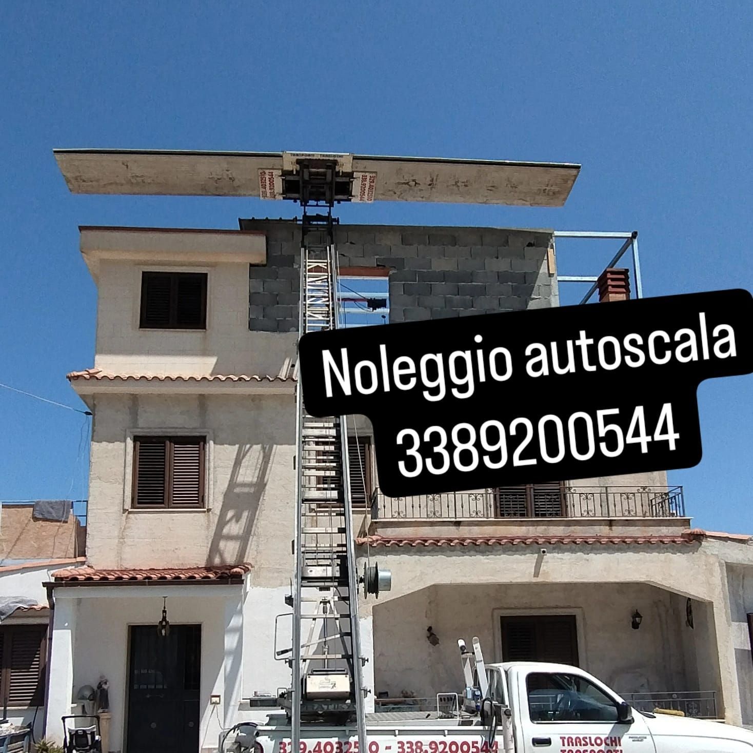 Un'autoscala (ascensore aereo) solleva un oggetto di grandi dimensioni sul tetto di un edificio. È indicato il numero di noleggio.