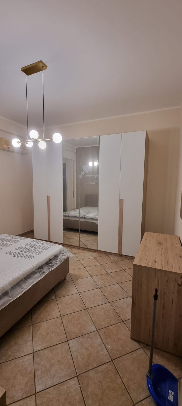Camera da letto con armadio bianco, cassettiera marrone chiaro, letto e pavimento piastrellato.