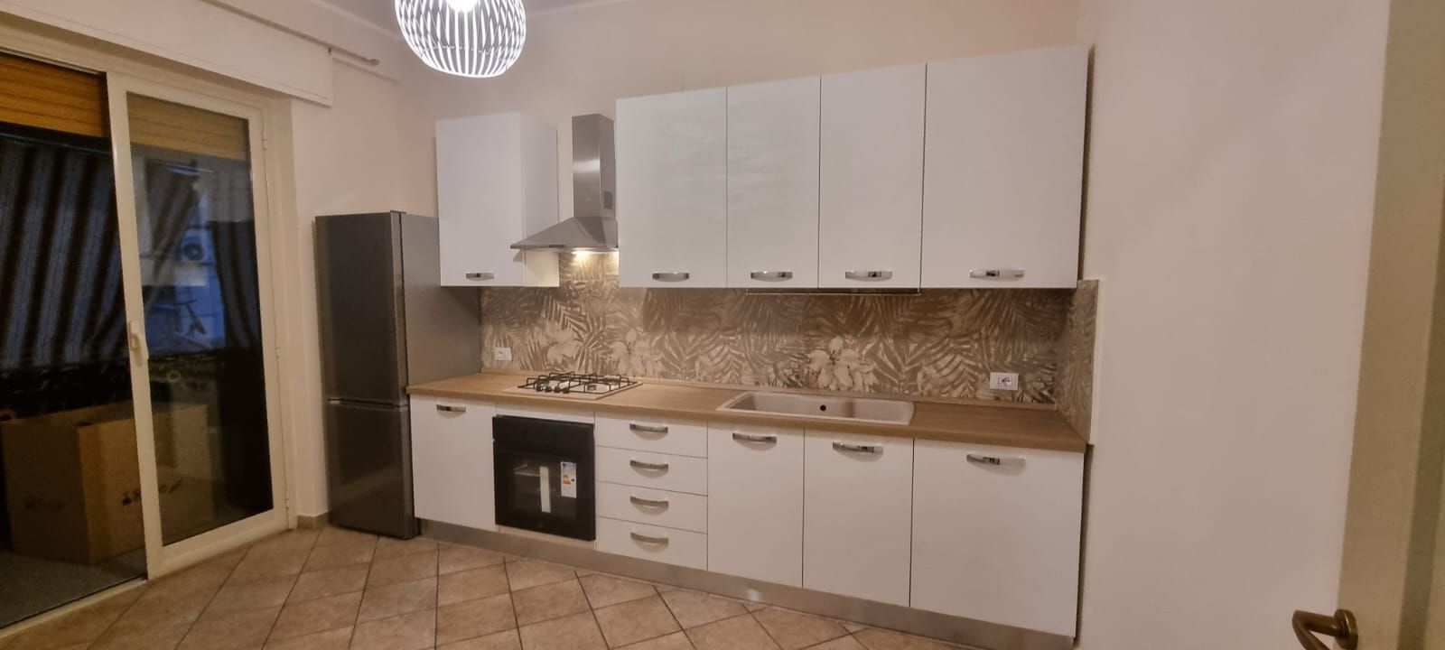 Una moderna cucina bianca con mobili, elettrodomestici e paraschizzi piastrellato.