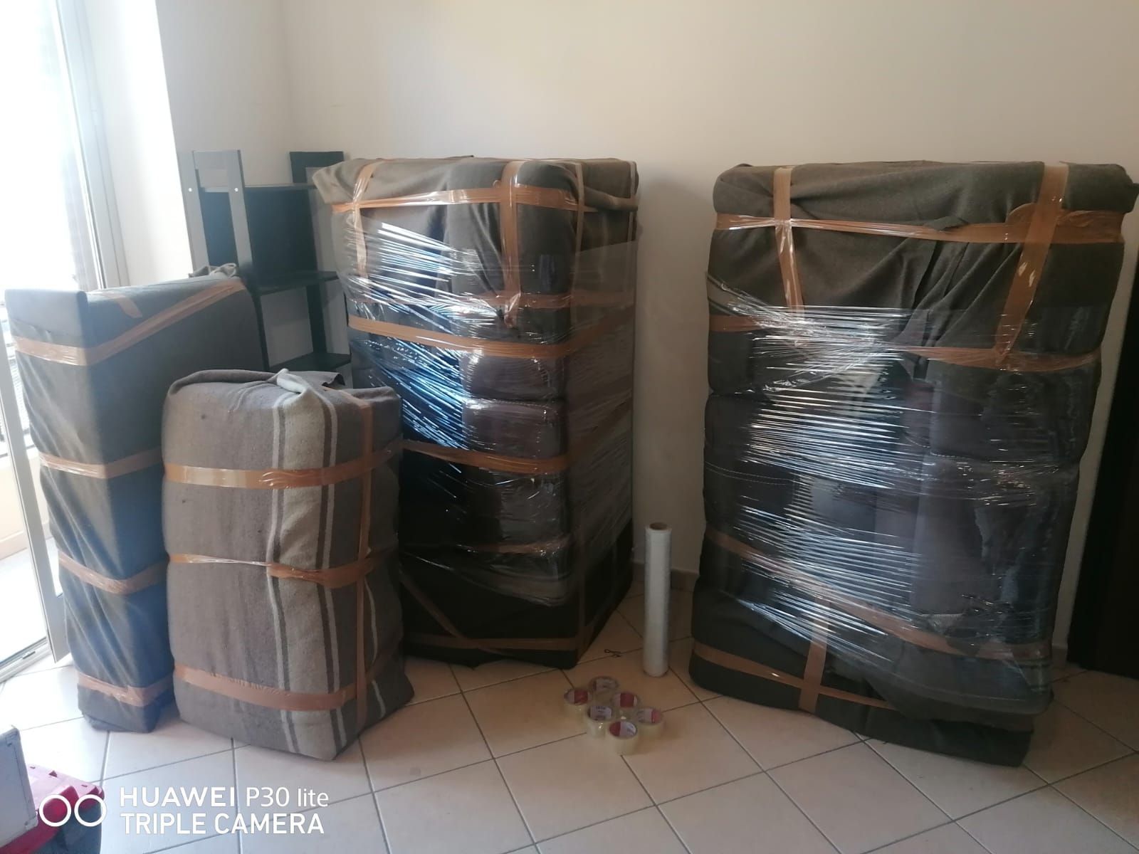 Mobili imballati e impilati in una stanza, pronti per il trasloco. Tessuto scuro con nastro adesivo e pellicola trasparente.