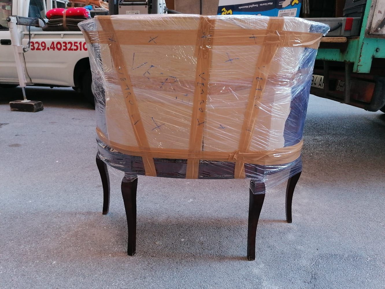 Una sedia avvolta in plastica e nastro adesivo, pronta per il trasporto. Gambe scure, schienale chiaro.