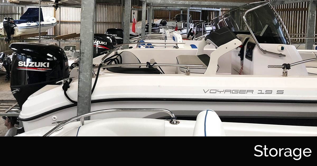 Boat storage area with several white motorboats parked indoors, including a black outboard motor in front