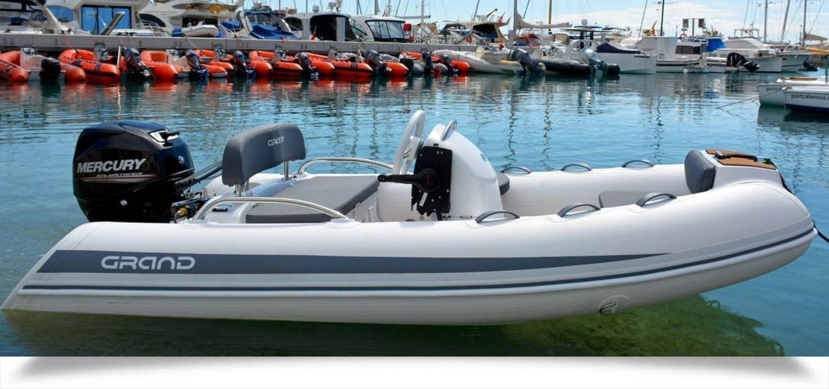Gray inflatable motorboat docked at a marina with calm blue water and moored boats in the background