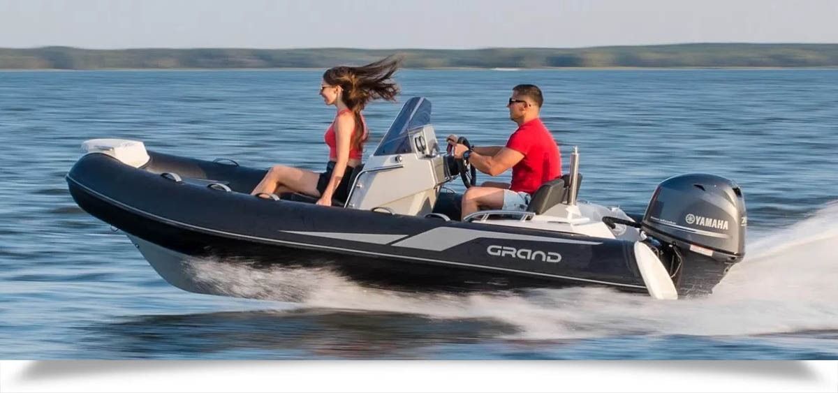 Two people ride a black inflatable speedboat on calm water, with one person steering and another seated behind.