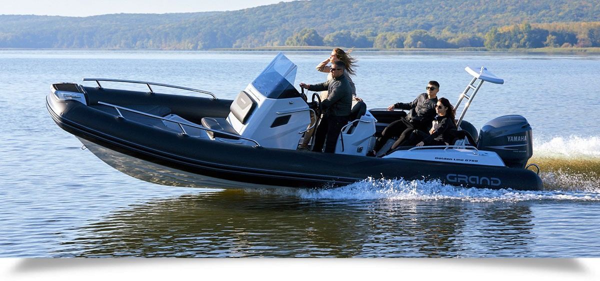 Two people ride a black inflatable boat on a calm lake with forested hills in the background