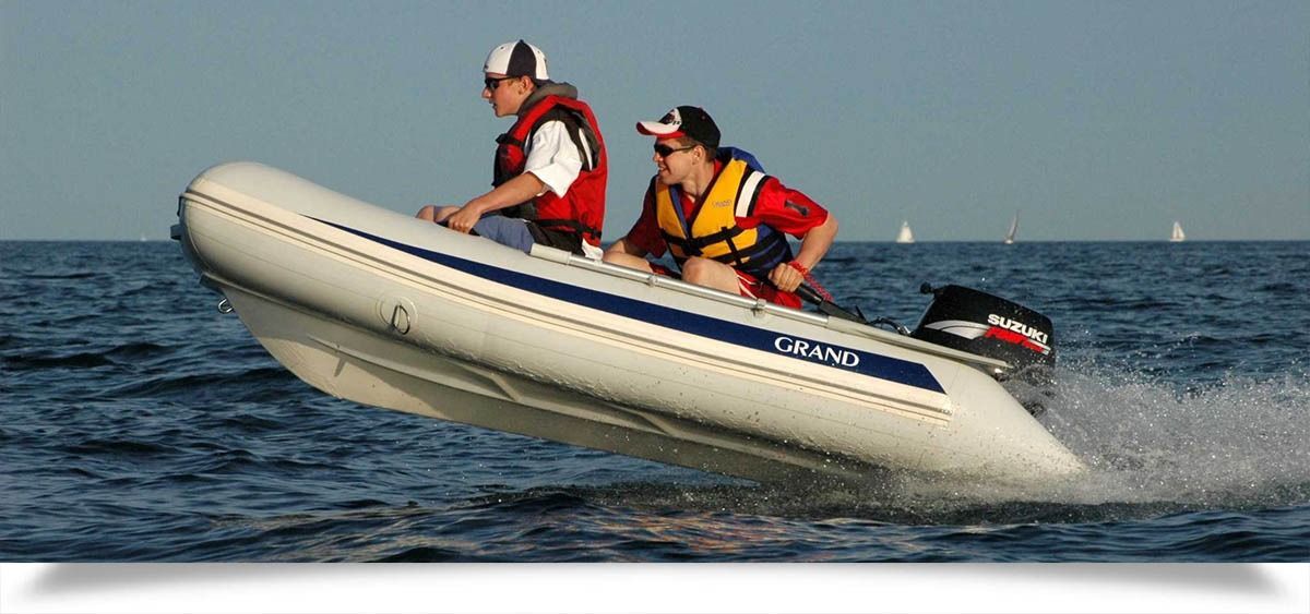Two people in life jackets riding a white inflatable boat over the ocean
