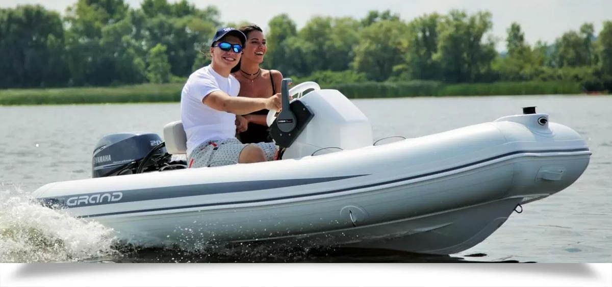 Two people ride a white inflatable speedboat across a calm lake, creating a spray wake.
