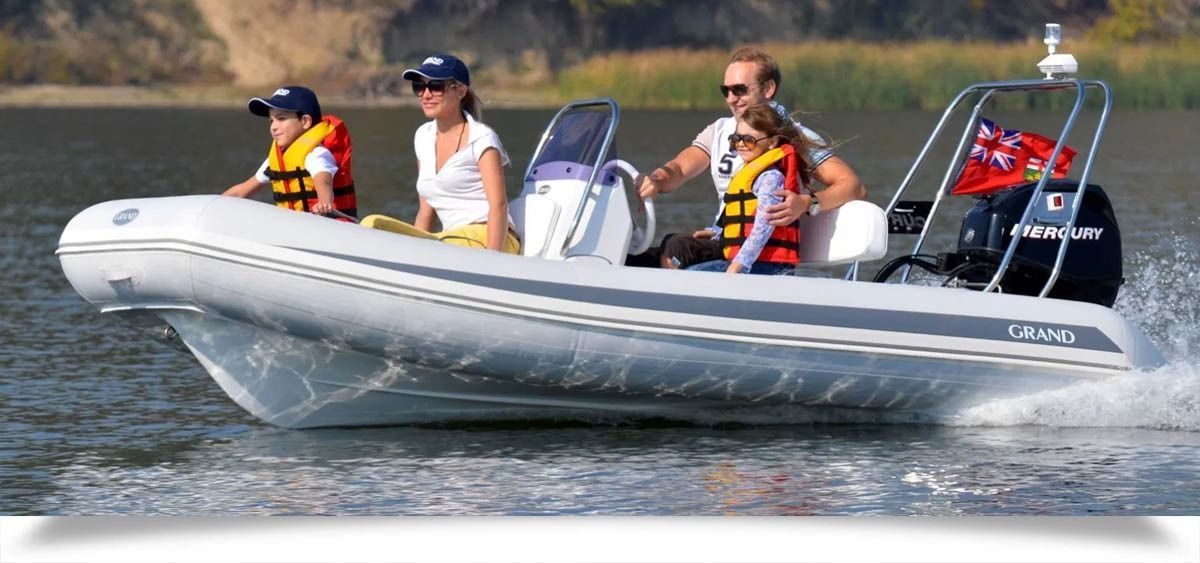 Four people ride in a gray inflatable motorboat on choppy water, wearing life jackets.