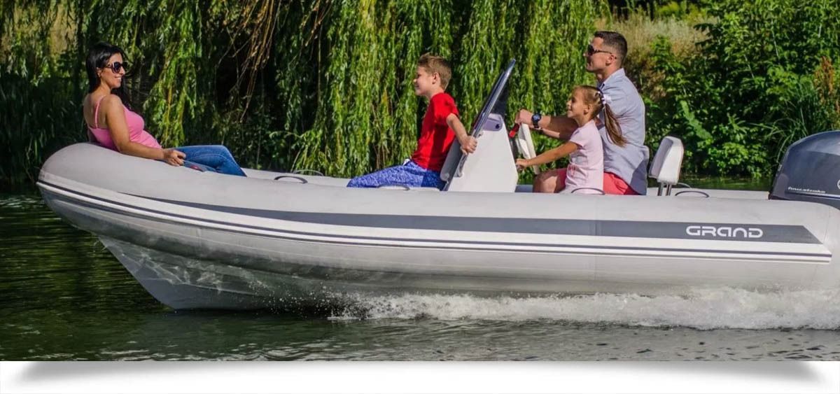 Four people riding in a gray inflatable grand silver line 470 boat on calm water near green reeds