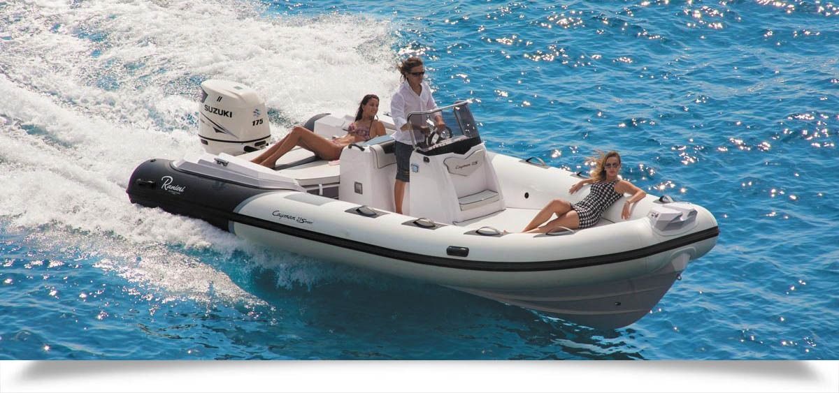 Two people riding a small white speedboat on bright blue water, leaving a foamy wake.