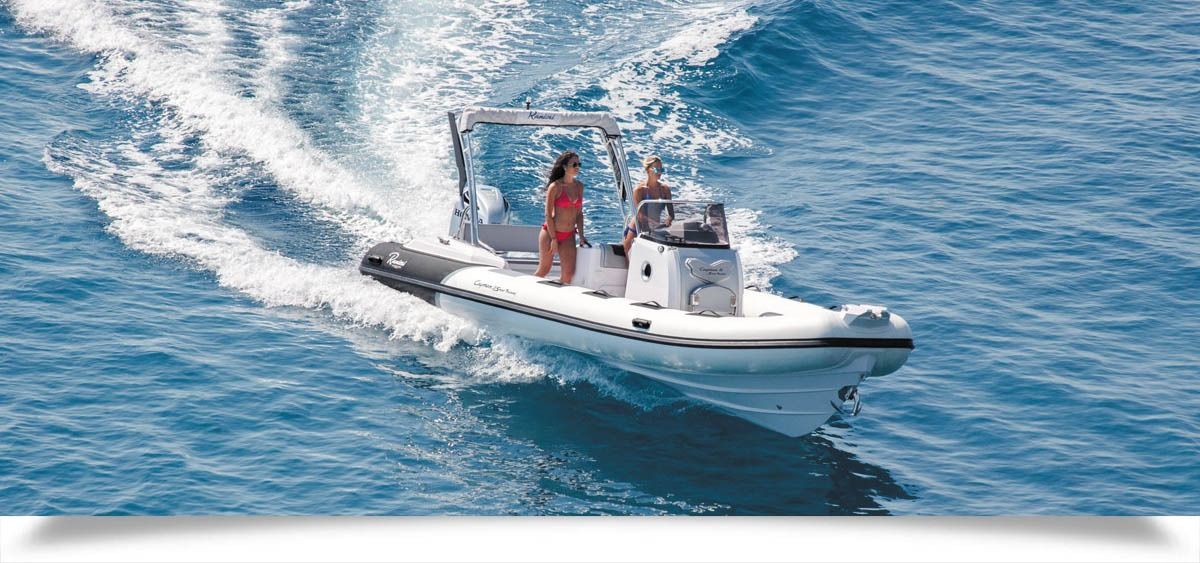 Two people on a white motorboat speeding across blue water, leaving a foamy wake