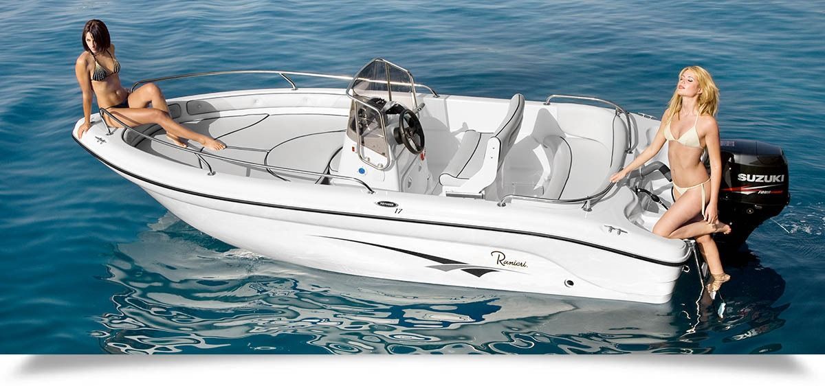 Two women posing on a white ranieri voyager 17 speedboat in blue water, with a small dog at the center.