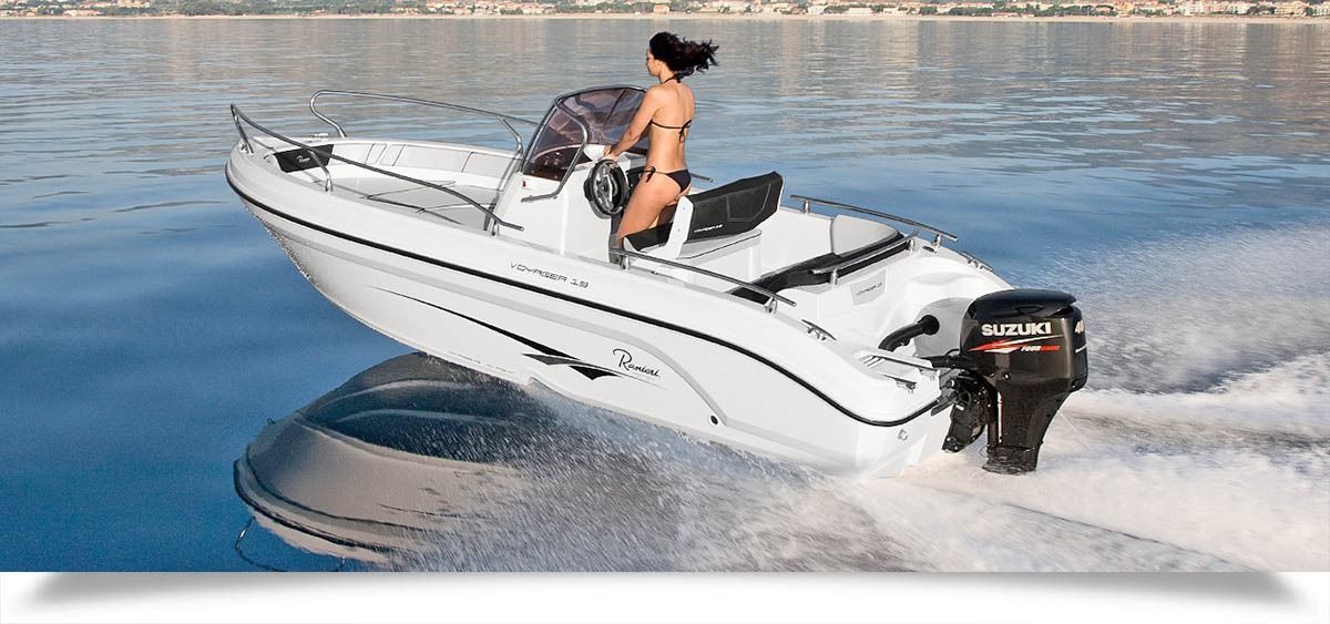 Motorboat speeding across calm water, leaving a wake, with a person standing at the helm