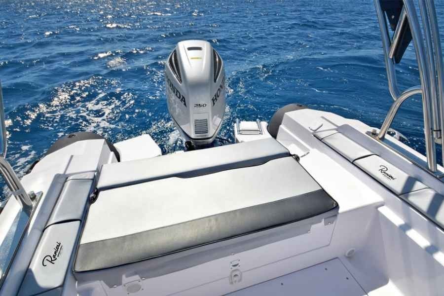 Boat deck with cushioned seating and an outboard motor on the open ocean