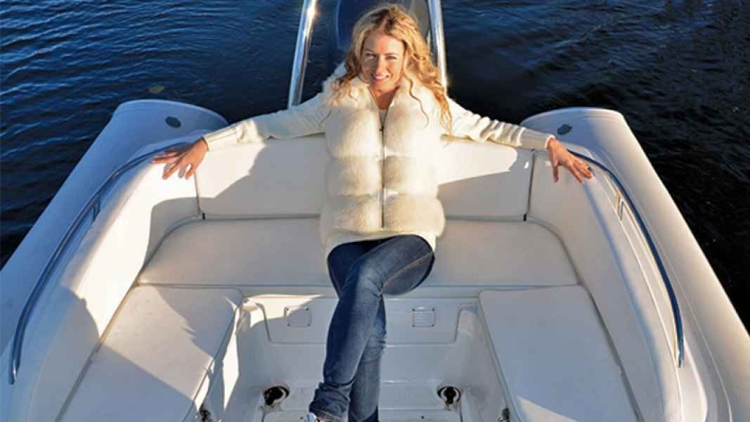 Woman lounging on a white boat deck with arms outstretched over dark water