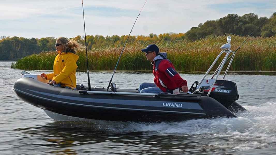 Two people riding a small inflatable grand silver line 370 boat on choppy water, one in yellow and one in red.