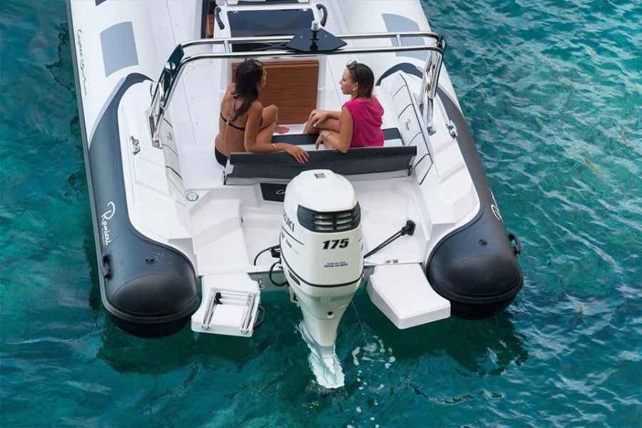 Two people sit on the stern of a white Ranieri Cayman 23 Sport Touring Rib inflatable boat over clear turquoise water.
