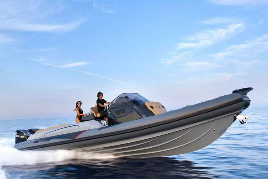 Two people riding a gray inflatable speedboat on calm blue water under a clear sky