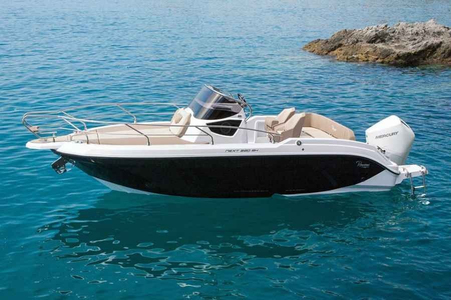 White and black speedboat floating on clear blue water near a rocky shoreline