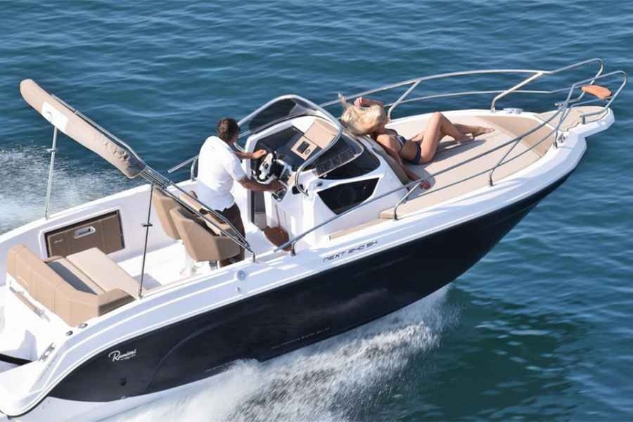 White motorboat cruising on blue water with two people on deck