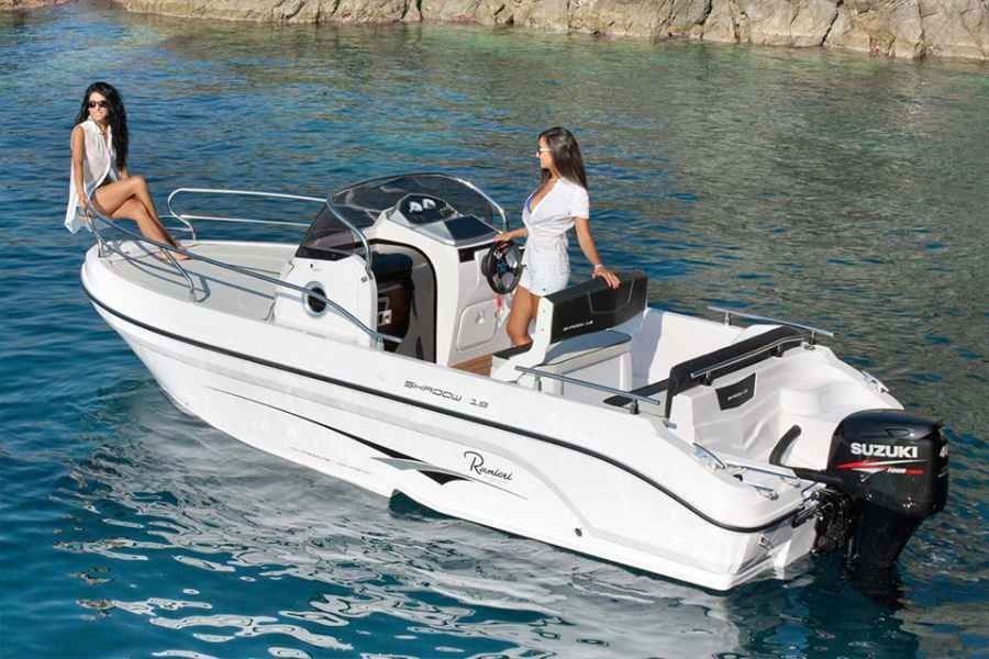 White motorboat with two women on calm blue water near rocky shore