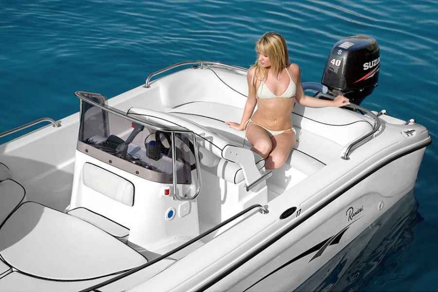 Woman sitting on a white motorboat on blue water, with the windshield open and outboard motor visible