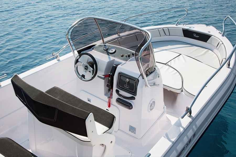 Small white motorboat cockpit with windshield, steering wheel, and cushioned seating on calm blue water