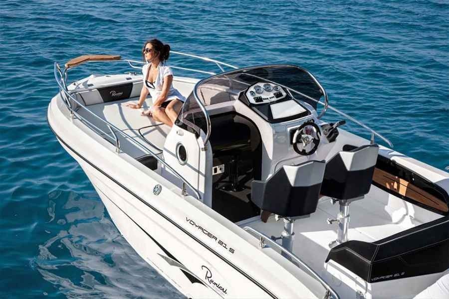 Woman sitting on a white speedboat on blue water, with the deck and helm visible