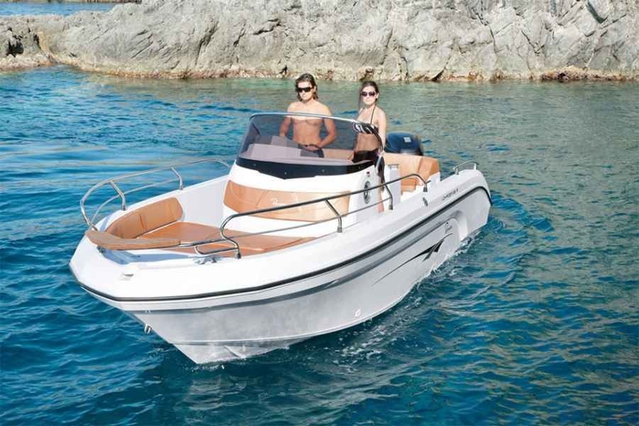 Two people on a white Ranieri Voager 23s motorboat cruising on clear blue water near rocky shore
