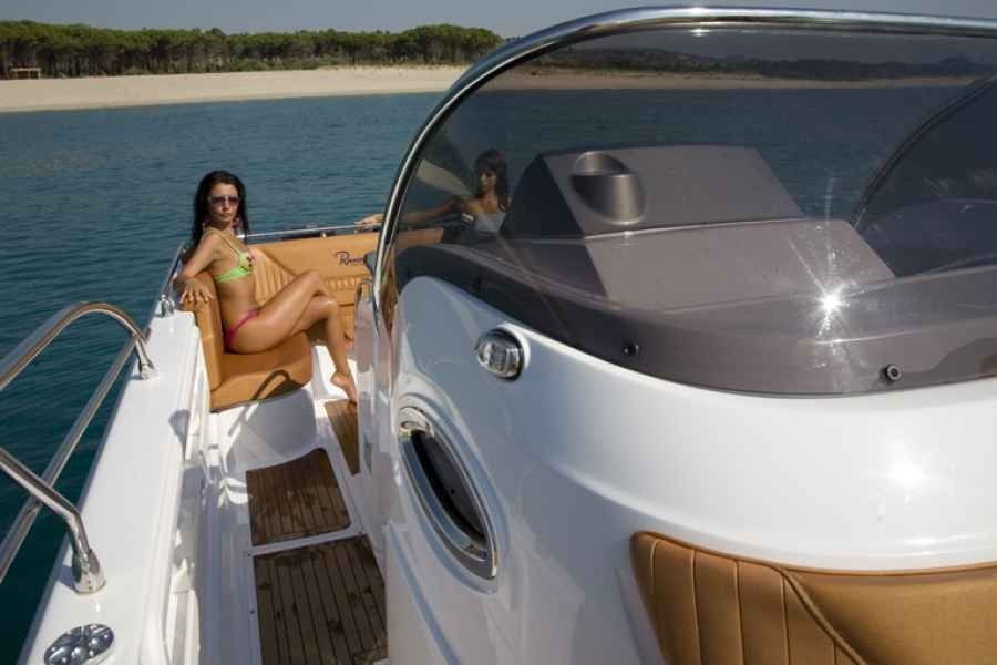 Woman relaxing on a white ranieri voyager 30 Sport deck with tan cushions, near a calm blue coastline