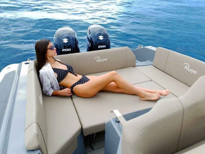 Woman reclining on a beige boat sunpad beside twin outboard motors on calm blue water