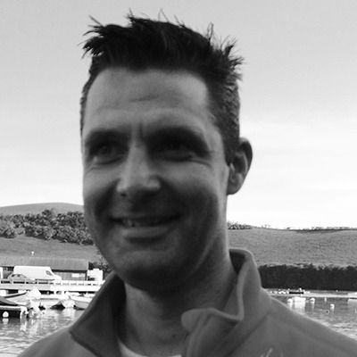 Smiling man in a collared shirt at a marina with boats and hills in the background