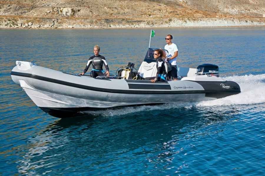 Speedboat with three people riding on blue water near a rocky shoreline