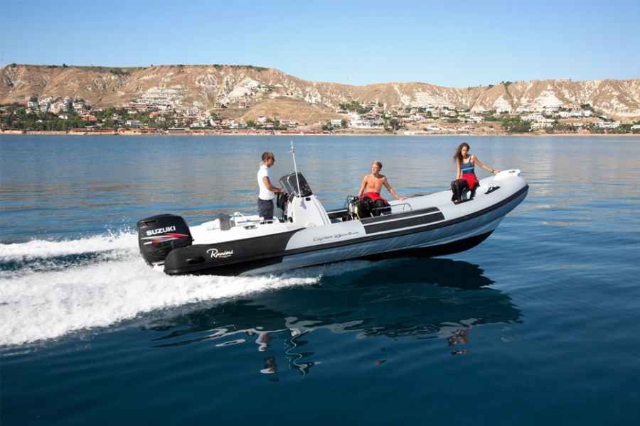 Speedboat with three people cruising on calm blue water near a rocky shoreline