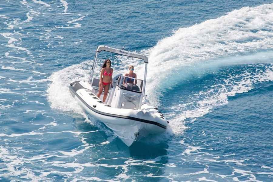 Speedboat carving a sharp turn on blue water, spraying white wake, with two people aboard.