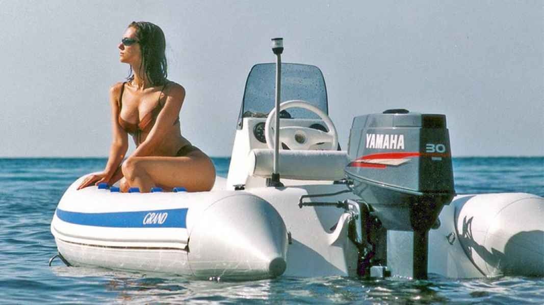 Woman sitting on a white inflatable boat beside a Yamaha outboard motor on calm blue water