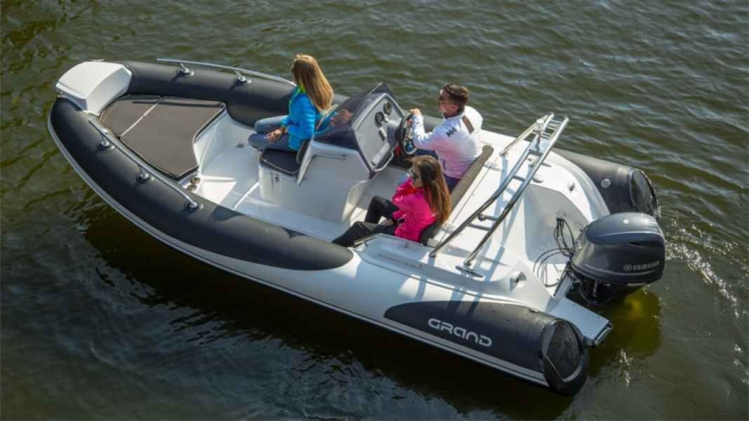Three people riding in a gray inflatable motorboat on calm green water
