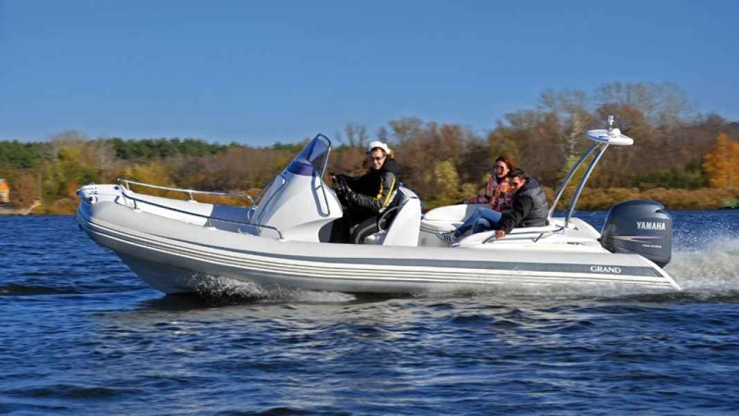 White motorboat with two people cruising on a blue lake near a wooded shoreline