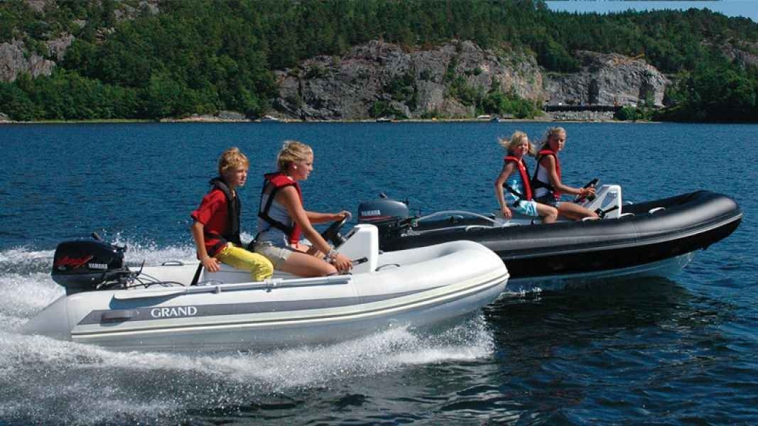 Two small motorboats on blue water, each carrying two people, near a forested rocky shoreline.